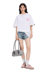 Woman wearing a white blurred rose graphic tee paired with distressed denim shorts and pink sneakers
