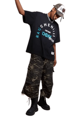 Model wearing IDontSmoke SS25 Arch Logo Tee black graphic t-shirt with camo pants and black boots