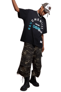 Model wearing IDontSmoke SS25 Arch Logo Tee black graphic t-shirt with camo pants and black boots