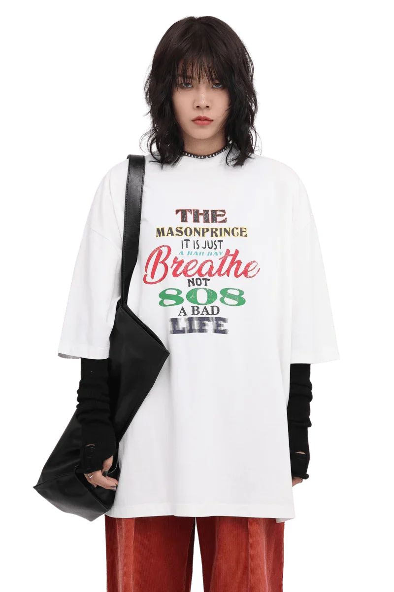White Masonprince 808 Breathe Tee with multicolor text worn by model with black layered sleeves and black bag