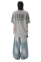 Back view of a person wearing a gray Masonprince reversed style tee with graphic print and loose faded jeans