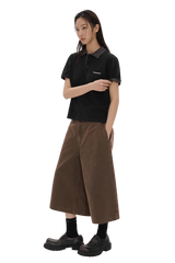 Woman wearing Masonprince SS25 Polo Tee in black paired with wide brown cropped pants and black shoes
