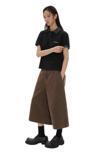 Woman wearing Masonprince SS25 Polo Tee in black paired with wide brown cropped pants and black shoes