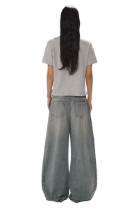 Back view of model wearing Masonprince SS25 Polo Tee in gray with wide leg denim jeans