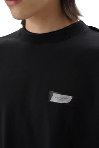 Close-up of black Masonprince SS25 Tape Tee with small white label on chest worn by model