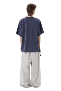 Back view of model wearing Masonprince SS25 Tape Tee navy short sleeve shirt with loose white pants