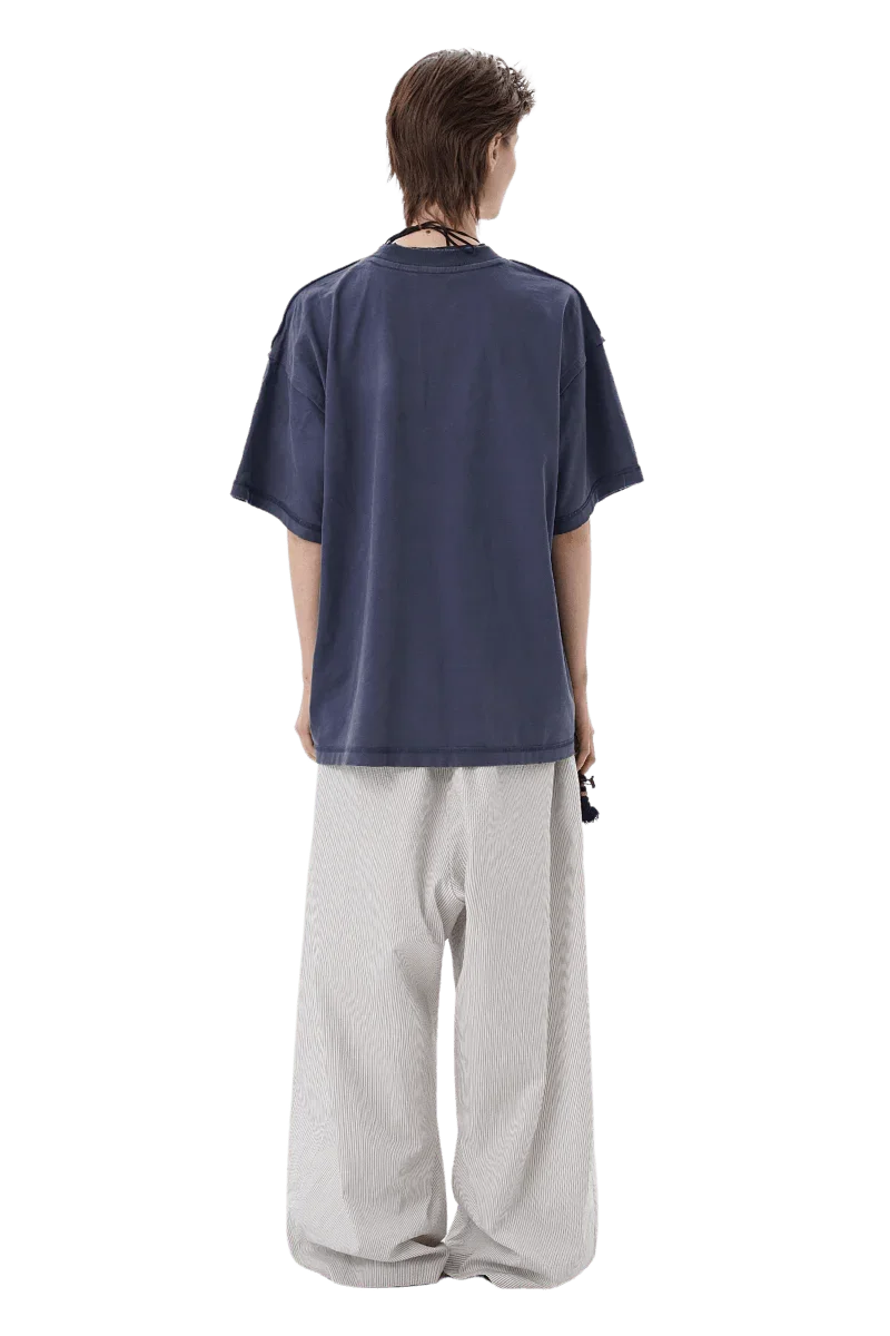 Back view of model wearing Masonprince SS25 Tape Tee navy short sleeve shirt with loose white pants