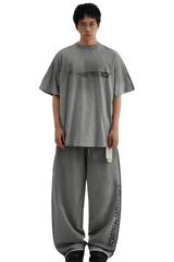 Model wearing gray Masonprince Tag Drop Tee with matching loose pants on black background