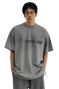 Masonprince Tag Drop Tee in gray worn by model with glasses featuring bold logo print on front