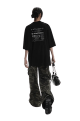 Back view of a person wearing black Masonprince WashTag Tee with white print and camo pants