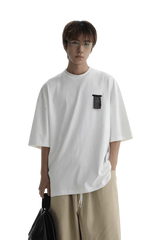 Model wearing a white Masonprince WashTag Tee with a black tag detail on the chest and beige pants