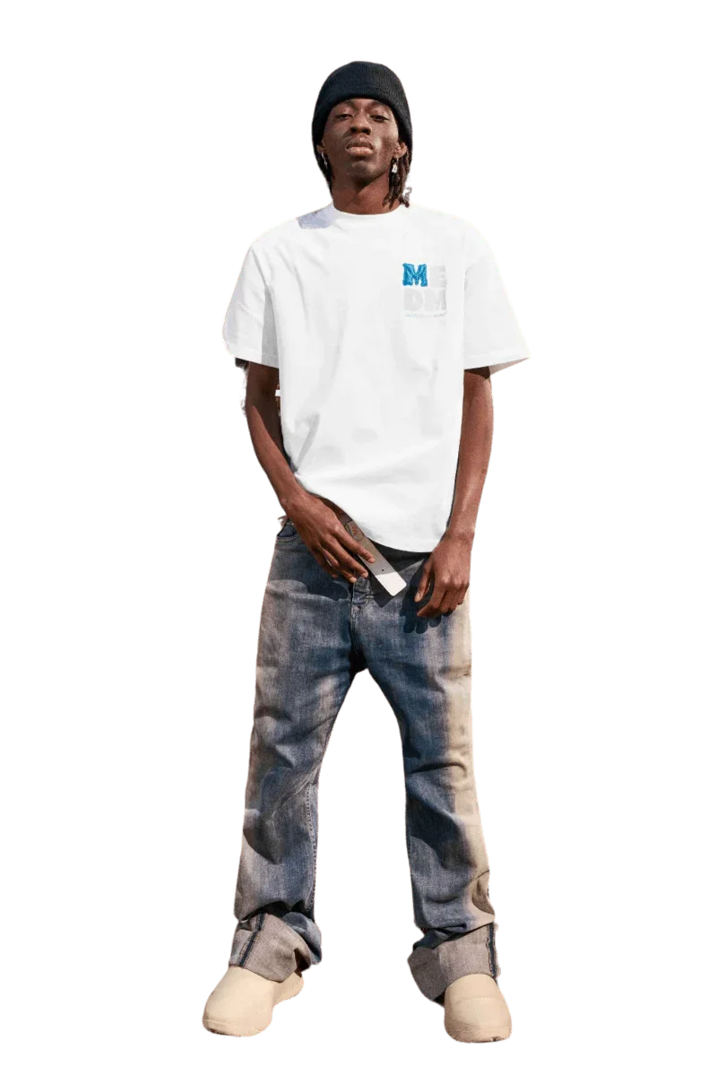 Model wearing the MEDM Badge Tee in white with blue logo, paired with distressed jeans.