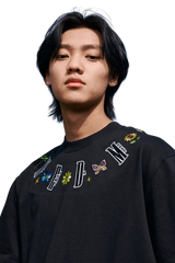 Young man wearing black MEDM Butterfly Necklace Embroidery Tee with colorful butterfly and floral designs around the neckline