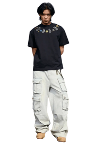 Man wearing black MEDM Butterfly Necklace Embroidery Tee with colorful embroidered design and white cargo pants