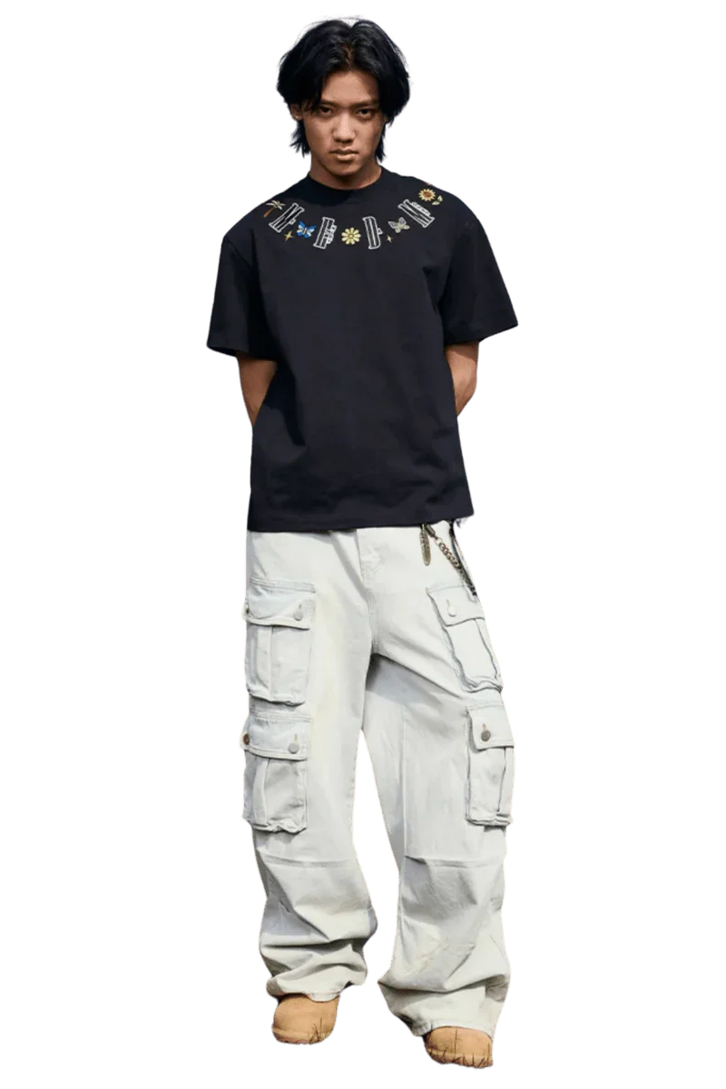 Man wearing black MEDM Butterfly Necklace Embroidery Tee with colorful embroidered design and white cargo pants