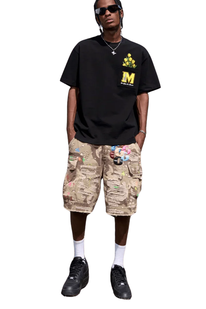 Man wearing a black MEDM Pixelated Flower Pocket Tee by Mr Enjoy Da Money with beige camo cargo shorts and black sneakers