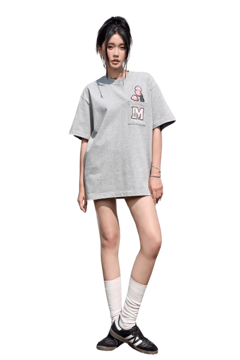 Model wearing a gray MEDM Pixelated Flower Pocket Tee by Mr Enjoy Da Money with pink flower graphic and letter M patch
