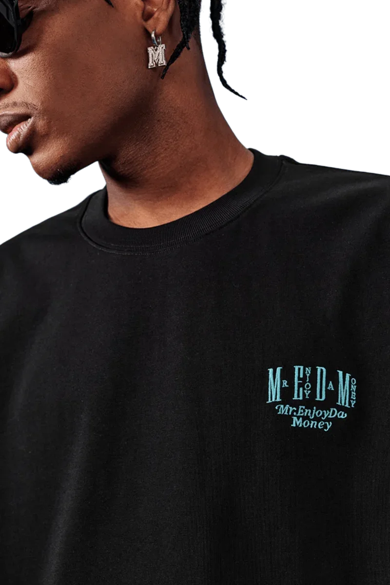 Close-up of MEDM SS25 Basic Embroidery Tee in black featuring Mr Enjoy Da Money logo on chest
