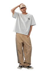 Model wearing the MEDM SS25 Basic Embroidery Tee in gray paired with khaki jeans and a cap