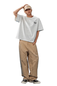 Model wearing the MEDM SS25 Basic Embroidery Tee in gray paired with khaki jeans and a cap