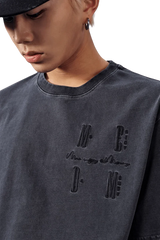 Model wearing the MEDM SS25 Basic Logo Washed Tee in dark fabric with embroidered details