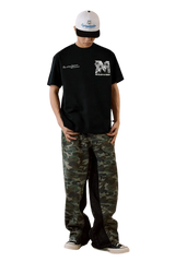 Model wearing MEDM SS25 Big M Daisy Print Tee in black with camo pants and a stylish cap