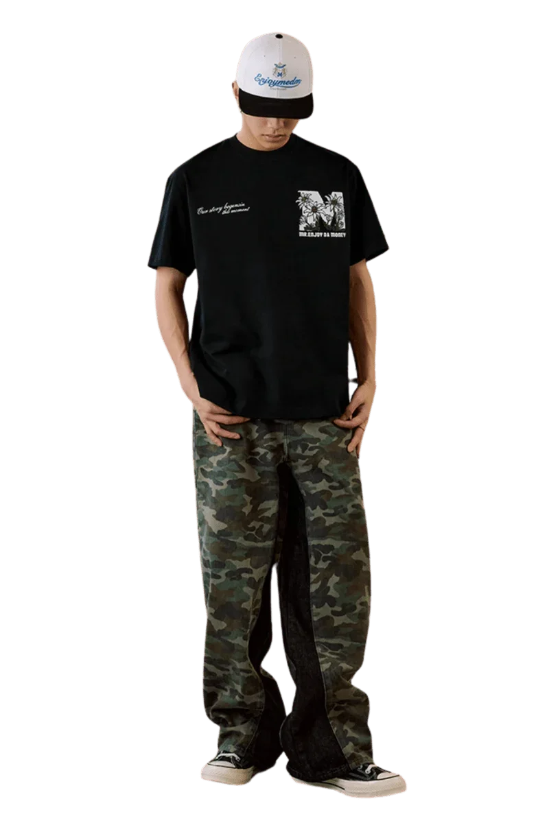 Model wearing MEDM SS25 Big M Daisy Print Tee in black with camo pants and a stylish cap