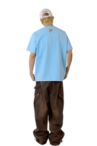 Back view of man's light blue MEDM SS25 Cat Velcro Embroidery Tee paired with casual brown cargo pants