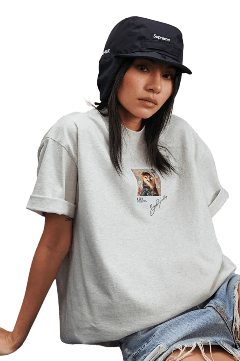 Stylish woman wearing a MEDM SS25 Dog Polaroid Tee in grey, paired with a black Supreme hat