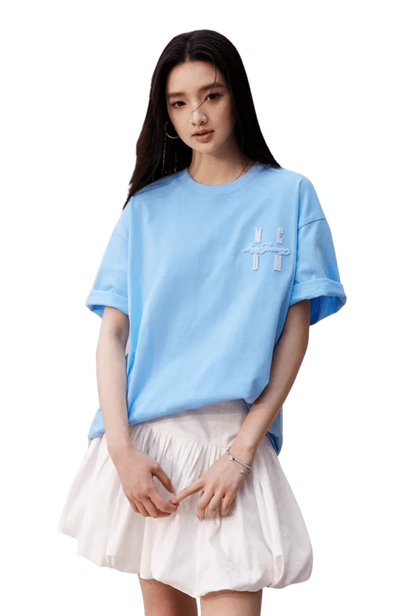 Model wearing a light blue MEDM SS25 Felt Embossed Basic Tee paired with a white skirt
