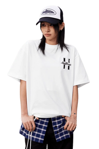 Model wearing a white MEDM SS25 Felt Embossed Basic Tee layered over a plaid shirt