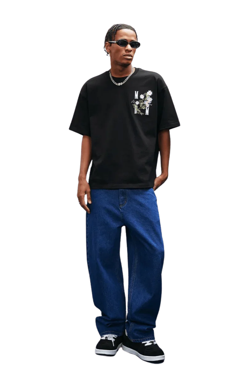 Model wearing MEDM SS25 Floral Embroidery Tee in black with jeans and sneakers, showcasing casual streetwear style.