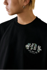Close-up of the MEDM SS25 Floral Felt Embossed Tee featuring vibrant floral embroidery on a black shirt