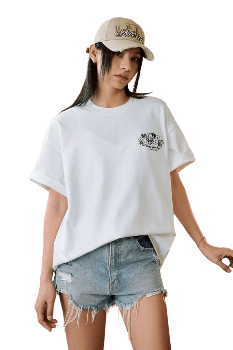 Model wearing MEDM SS25 Floral Felt Embossed Tee with denim shorts and a stylish cap