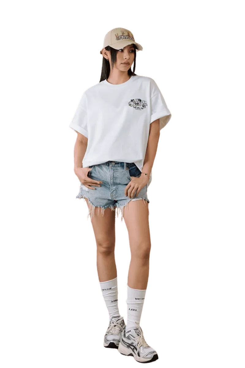 Model wearing MEDM SS25 Floral Felt Embossed Tee with denim shorts and a cap for a casual look