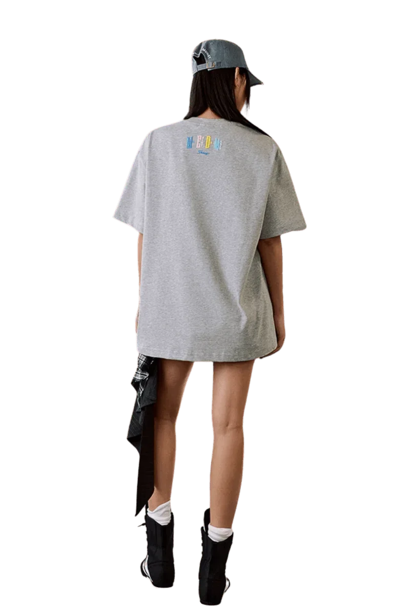 Model wearing MEDM SS25 Macaron Velvet Embossed Tee in gray from the back, styled with a denim cap