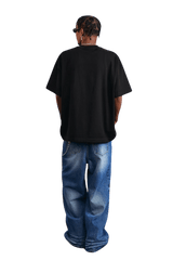 Back view of a model wearing a black MEDM SS25 Serendipity Embroidery Tee with loose jeans