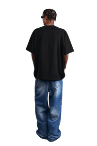 Back view of a model wearing a black MEDM SS25 Serendipity Embroidery Tee with loose jeans