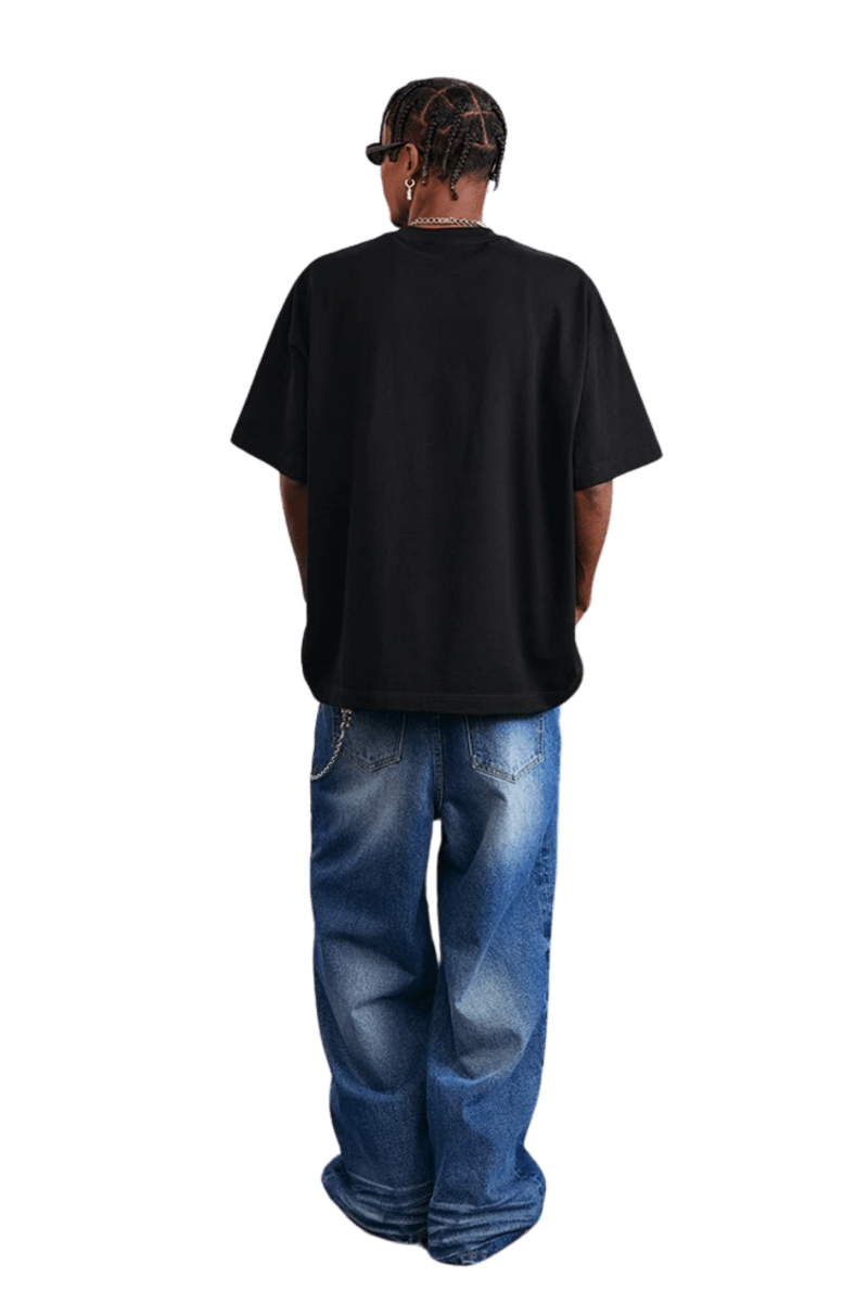 Back view of a model wearing a black MEDM SS25 Serendipity Embroidery Tee with loose jeans