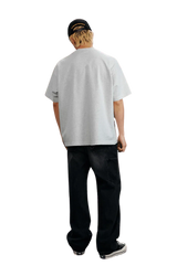 Back view of the MEDM SS25 Serendipity Embroidery Tee in light gray, stylishly paired with dark jeans