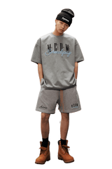 Fashion model wearing MEDM SS25 Serendipity Embroidery Tee with gray shorts and boots