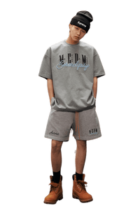 Fashion model wearing MEDM SS25 Serendipity Embroidery Tee with gray shorts and boots