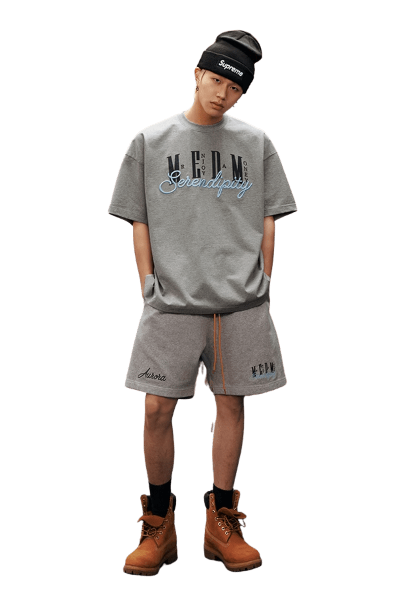 Fashion model wearing MEDM SS25 Serendipity Embroidery Tee with gray shorts and boots