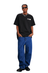 Model wearing MEDM SS25 The Time Basic Logo Tee in black with relaxed fit and blue jeans for a casual look
