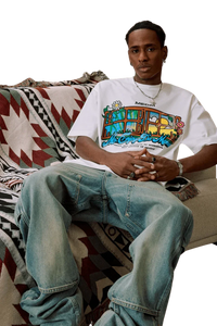 Man wearing white MEDM Window Spring Tee with colorful graphic design sitting on patterned blanket