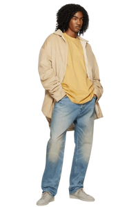 Model wearing Fear Of God Essentials SS23 Rubber Embossed Tee in mustard yellow with relaxed-fit jeans