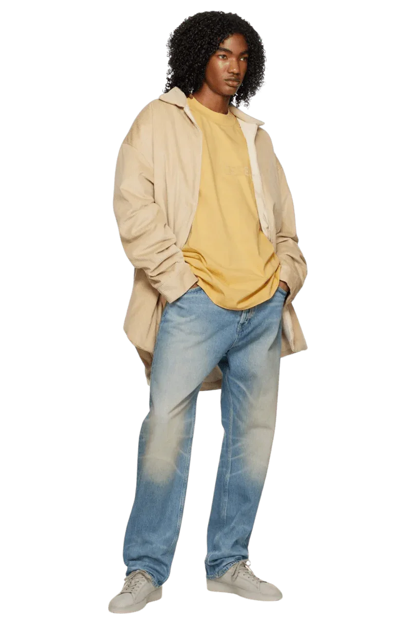 Model wearing Fear Of God Essentials SS23 Rubber Embossed Tee in mustard yellow with relaxed-fit jeans